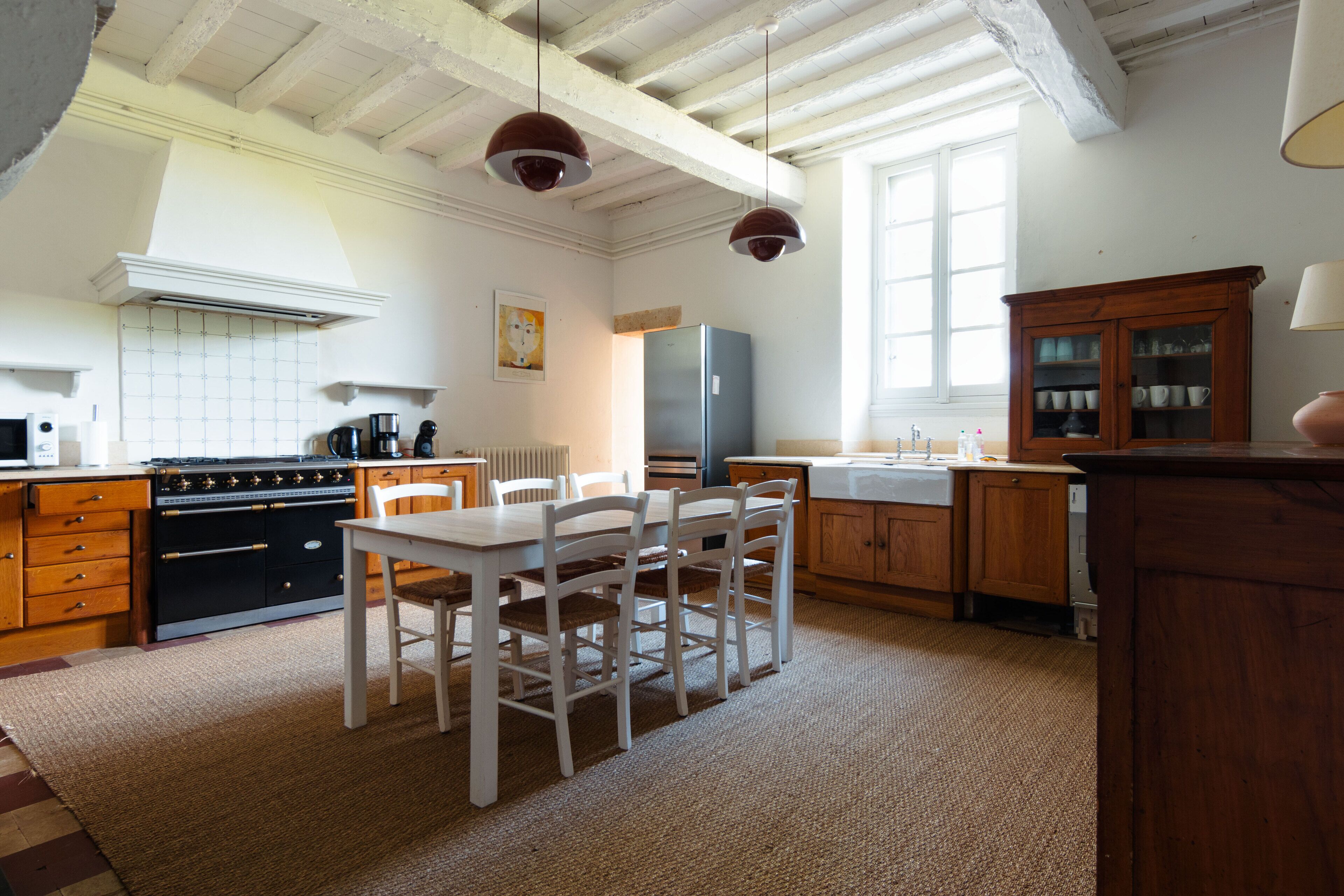 Una cocina con armarios de madera, una mesa blanca y lámparas colgantes.