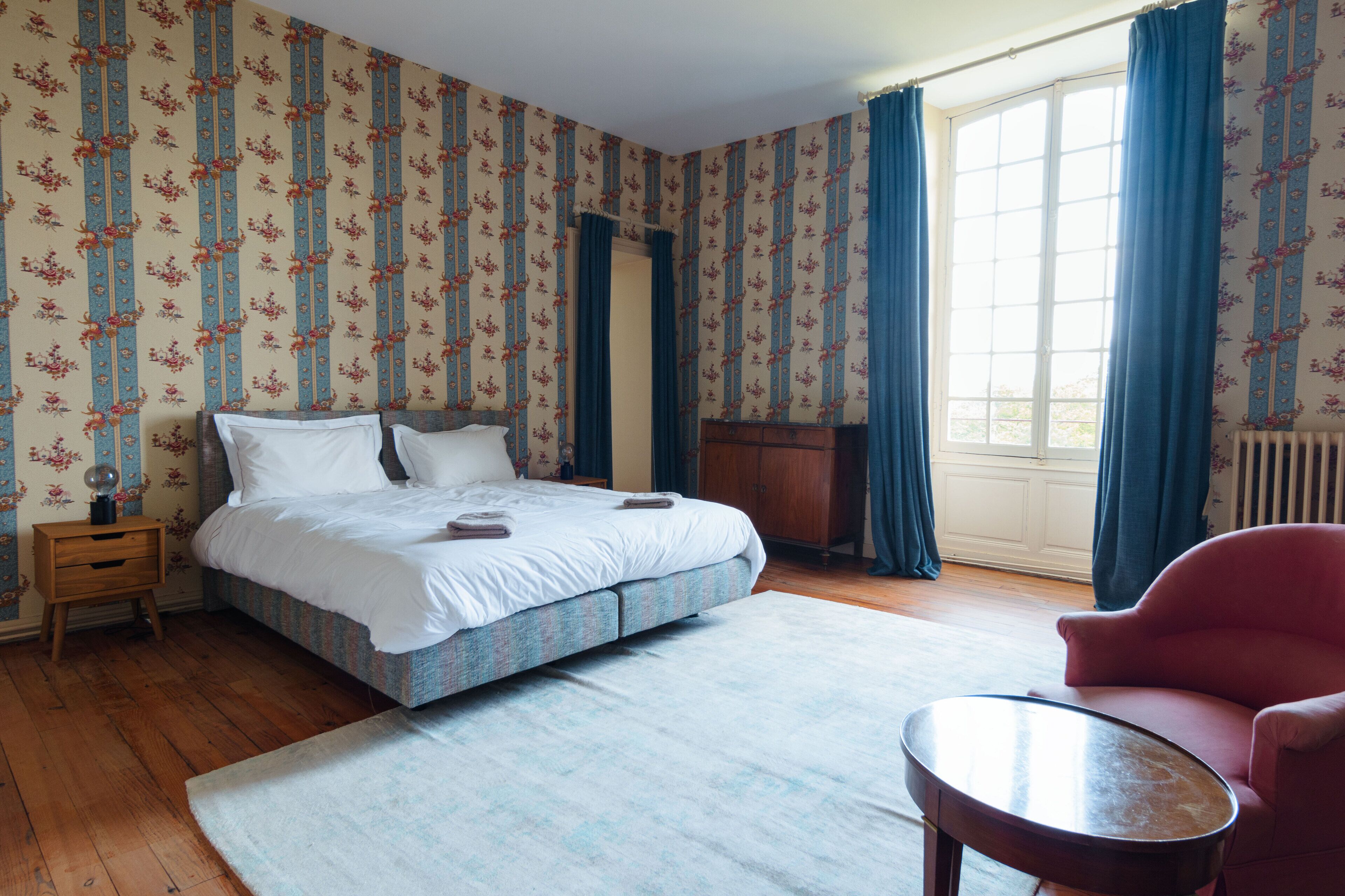 Une chambre à coucher avec un lit, une table de chevet, une chaise et une fenêtre avec des rideaux.
