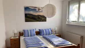 Ein Schlafzimmer mit einem hölzernen Bett, gestreifter Bettwäsche, zwei Nachttischen mit Lampen, einer hängenden Papierlaterne, einem Fenster mit Vorhängen und einem Landschaftsbild an der Wand.