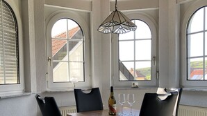 Ein Essbereich mit einem Holztisch und schwarzen Stühlen, einer hängenden Leuchte und großen Bogenfenstern.