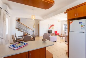 A modern kitchen with a central island, a dining area with a staircase, and a living room with a sofa and TV. - Queens Paradise 1 - Three Bedroom Villa, Sleeps 6 (Peyia)