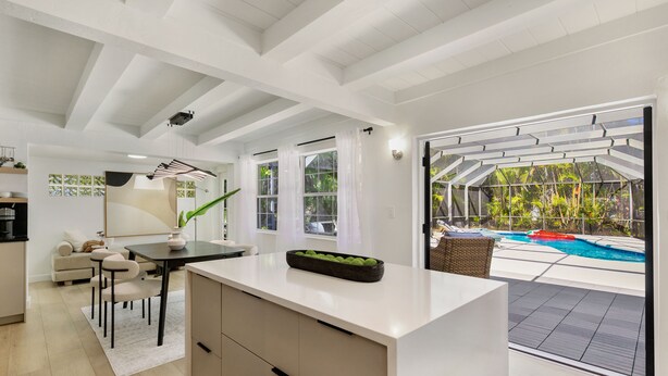 A modern kitchen with a dining area, large windows, and a view of an outdoor swimming pool.