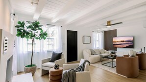 A modern living room with a large window, a potted plant, a sofa, a coffee table, and a flat-screen TV.
