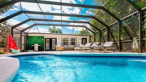 A covered swimming pool with lounge chairs, a slide, and a green wall.