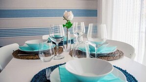 Une table dressée avec de l’argenterie bleue et blanche, des verres et un bouquet de roses blanches en guise de centre de table.