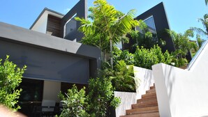 Un bâtiment moderne doté d’un escalier, entouré d’une végétation luxuriante et surplombé d’un ciel bleu azur.