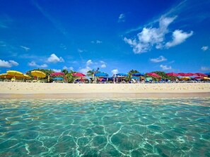 A beach with clear turquoise water and a row of colorful umbrellas.