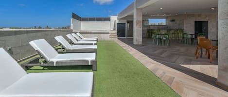 A rooftop lounge area with sun loungers and a bar area with chairs.