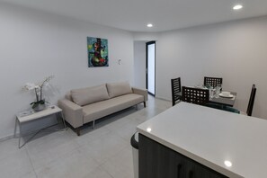 A modern living room with a sofa, a dining table with chairs, and a kitchen area.