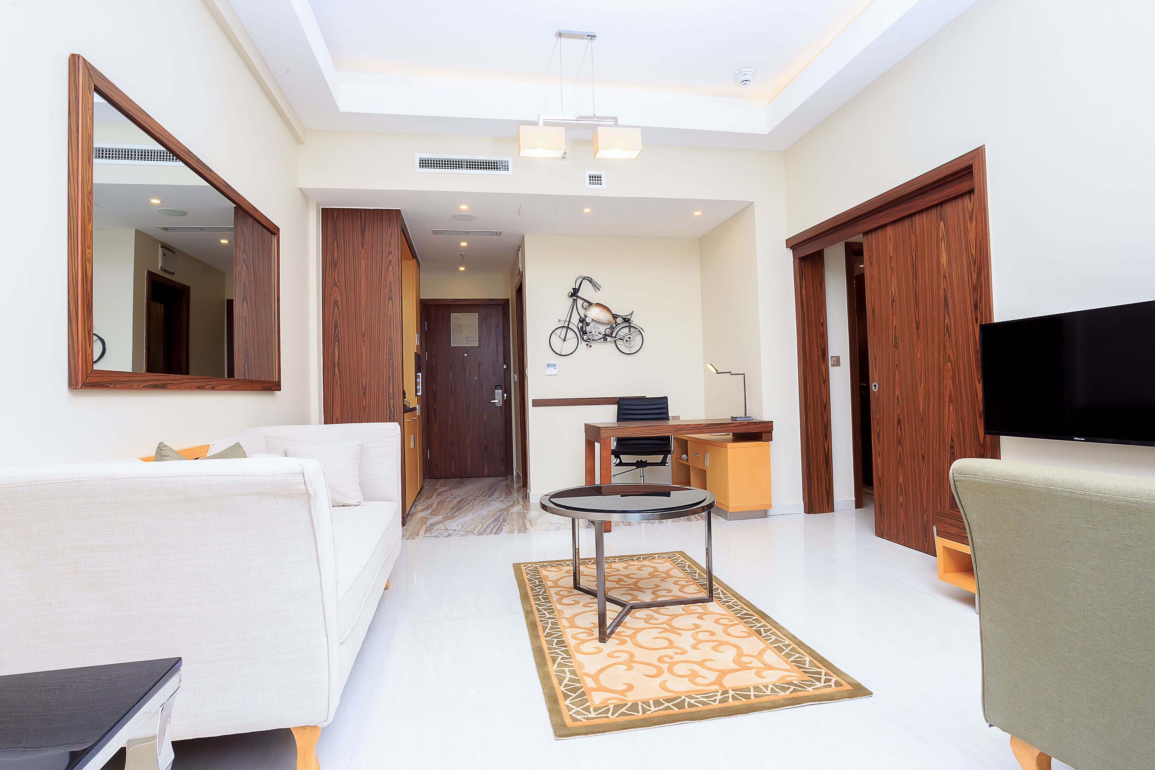 A modern living room with a sofa, a coffee table, and a TV. There is a bicycle wall art and a wooden door.
