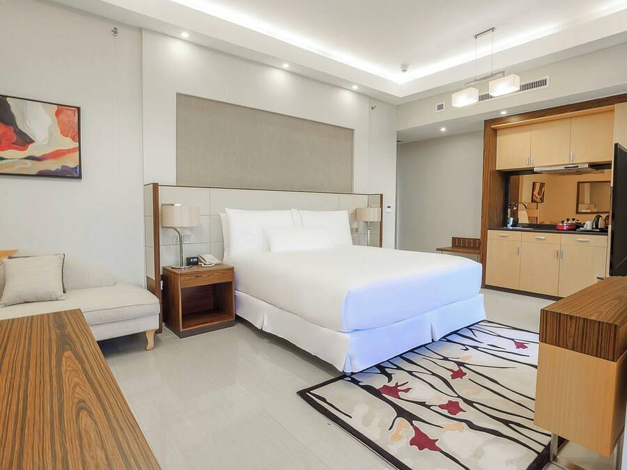 Una habitación de hotel moderna con una cama grande, un escritorio, una silla, una mesita de noche, un televisor y un rincón americano.