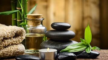 Un décor de spa avec un fond de bambous, une bouteille en verre bouchée d’un bouchon, des pierres noires, une bougie allumée et une plante verte.