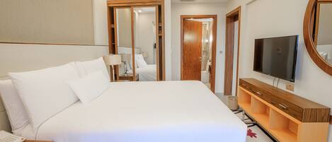 A hotel room with a large bed, a bedside telephone, a TV, and a wooden dresser.