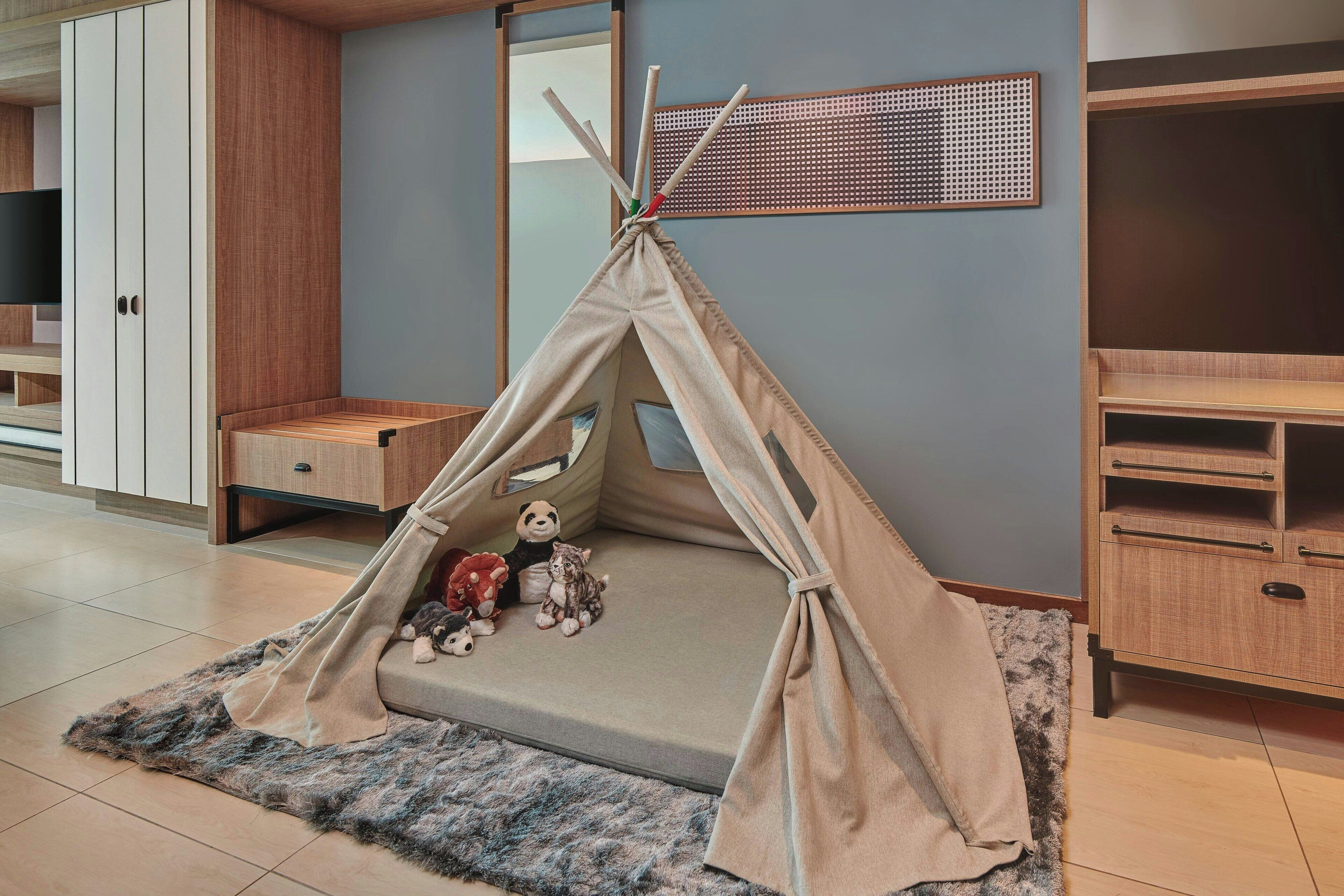 Una habitación con una estructura tipo tienda en tono beige sobre una alfombra, armarios de madera y un televisor a la izquierda.