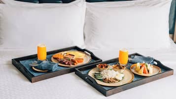 Una bandeja de desayuno ordenada sobre una cama con cabecera, mostrando una variedad de platos y un vaso de zumo de naranja.