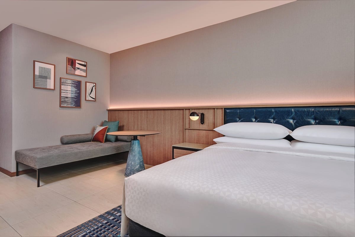 A hotel room with a bed, a sofa, a small table, and wall art.
