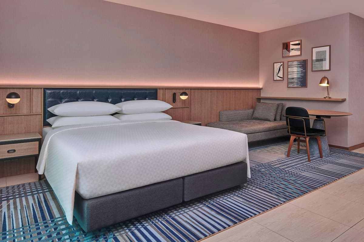 A modern hotel room with a large bed, a desk, and a chair.
