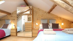 Ein gemütliches Schlafzimmer im Dachgeschoss mit zwei Betten, Holzbalken und einer Steinwand.