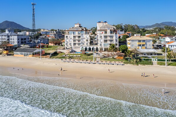 Un hotel frente a la playa con varias edificaciones, una playa de arena y un cielo azul despejado.