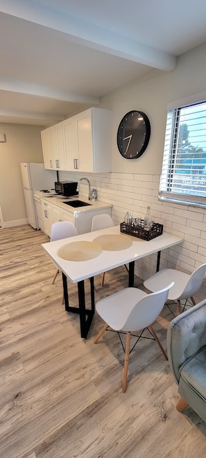 Una cocina moderna con armarios blancos, un reloj negro y un comedor con mesa y sillas.