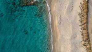 An aerial view of a beach with clear turquoise waters and a sandy shore.