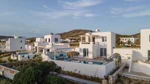 A modern white villa with a pool, surrounded by greenery and a mountainous backdrop.
