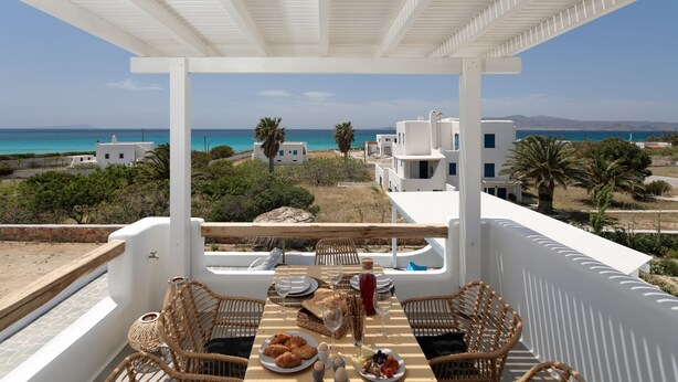 A terrace with a table set for dining, overlooking a coastal landscape with buildings and palm trees.