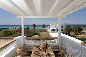 A terrace with a table set for dining, overlooking a coastal landscape with buildings and palm trees. - Villa Ester Unique Beachfront 4BR with Private Pool at Kastraki, Naxos (Naxos)
