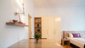 A modern bedroom with a wooden bed, bedside table, and a nightstand. There is a dining table with chairs and a potted plant in the center. - Vienna Residence, City Hall - Parliament #6411 (Vienna)