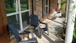 A covered patio with two Adirondack chairs, a white chair with a pumpkin decoration, and a brick wall. - Peaceful Scenic Pond & Home Close to Beach/Sports/Entertainment (Elberta)