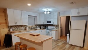 A modern kitchen with white cabinets, a wooden island with stools, a microwave, and a refrigerator. - Peaceful Scenic Pond & Home Close to Beach/Sports/Entertainment (Elberta)
