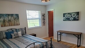 A bedroom with a bed, a bench, a window, and artwork on the walls. - Peaceful Scenic Pond & Home Close to Beach/Sports/Entertainment (Elberta)