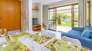 A dining area with a table set for four, a blue sofa, and a view of a garden through large sliding doors.
