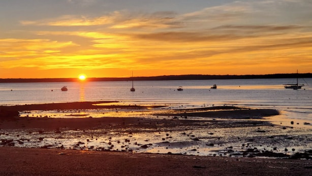 Um pôr do sol sobre uma praia com barcos e linhas costeiras rochosas.