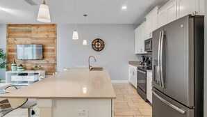 Eine moderne Küche mit Kochinsel, Edelstahlgeräten, Pendelleuchten und einer Wand aus Holzpaneelen.