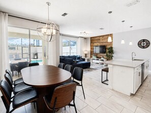 A modern kitchen with a dining area, a sofa, and a TV on the wall.