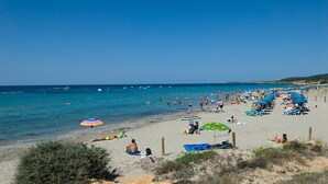 A beach with people sunbathing and swimming, umbrellas, and lounge chairs. - Villa Gecko by Villa Plus (Sant Tomas)