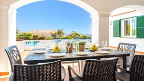 A terrace with a table set for dining, overlooking a pool and a view of a building with a red roof. - Villa Gecko by Villa Plus (Sant Tomas)