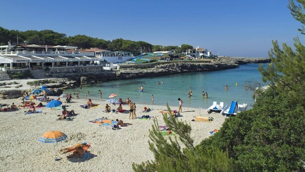 A beach with people sunbathing and swimming, a restaurant, and a boat dock.