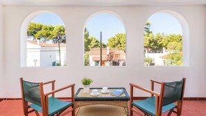 A room with three arched windows, a table with chairs, and a view of a residential area with trees and buildings.