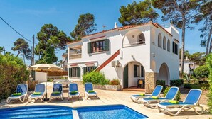 A two-story white villa with a swimming pool, outdoor seating, and a garden.