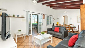 Ein geräumiger Wohnbereich mit einer Couch, einem Couchtisch und einem Esstisch. Eine Glastür öffnet sich zu einer Terrasse.