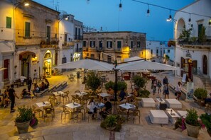 An outdoor café with tables and chairs, surrounded by buildings with balconies and windows. - Villa Aranceto by Villa Plus (San Vito dei Normanni)