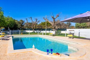 A rectangular swimming pool with a tiled edge, surrounded by a paved patio. There are lounge chairs and a covered area with an umbrella. - Villa Aranceto by Villa Plus (San Vito dei Normanni)