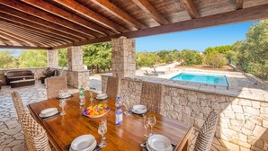 Un área de comedor al aire libre con pilares de piedra, techo de madera y vista a una piscina.