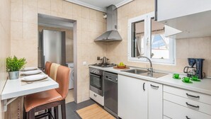 Una cocina compacta con comedor, horno empotrado, lavavajillas y ventana con vistas al exterior.