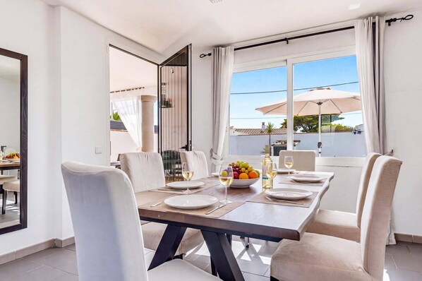 A dining area with a table set for four, a bowl of fruit, and wine glasses. - Villa Quimera by Villa Plus (Cala en Porter)