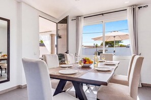 A dining area with a table set for four, a bowl of fruit, and wine glasses. - Villa Quimera by Villa Plus (Cala en Porter)