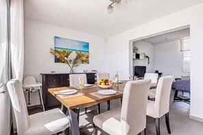 A dining area with a wooden table, white chairs, and a painting of a beach scene. - Villa Quimera by Villa Plus (Cala en Porter)