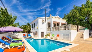 A pool area with lounge chairs and a purple umbrella. - Villa Karenessa by Villa Plus (Cala en Porter)